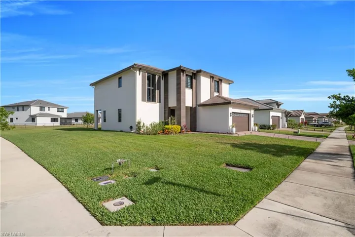 View of front facade featuring a garage, stucco siding, a front lawn, and driveway