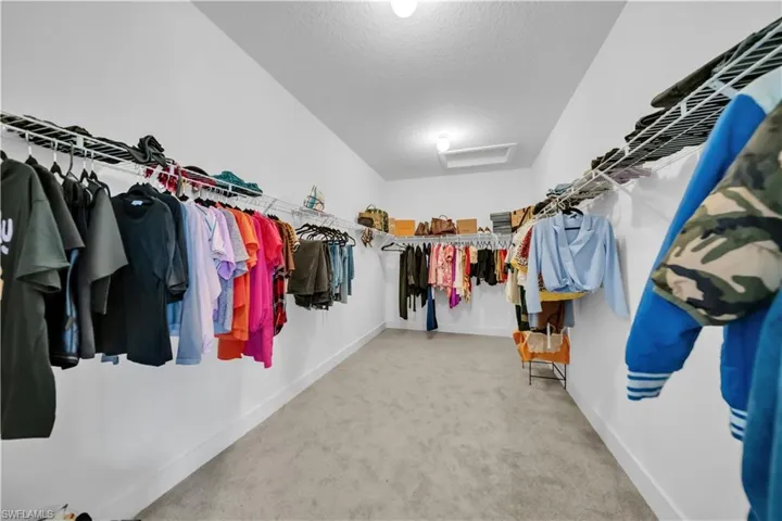 Walk in closet with attic access and light colored carpet