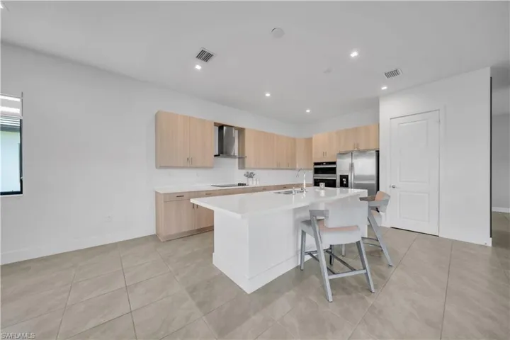 Kitchen with light brown cabinets, modern cabinets, a kitchen island with sink, a breakfast bar area, and light tile patterned floors