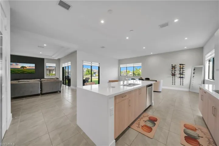 Kitchen featuring light brown cabinetry, open floor plan, light tile patterned floors, light stone countertops, and a center island with sink
