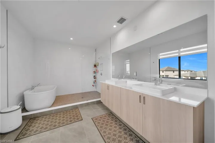 Full bathroom with double vanity, a walk in shower, light tile patterned flooring, a soaking tub, and recessed lighting