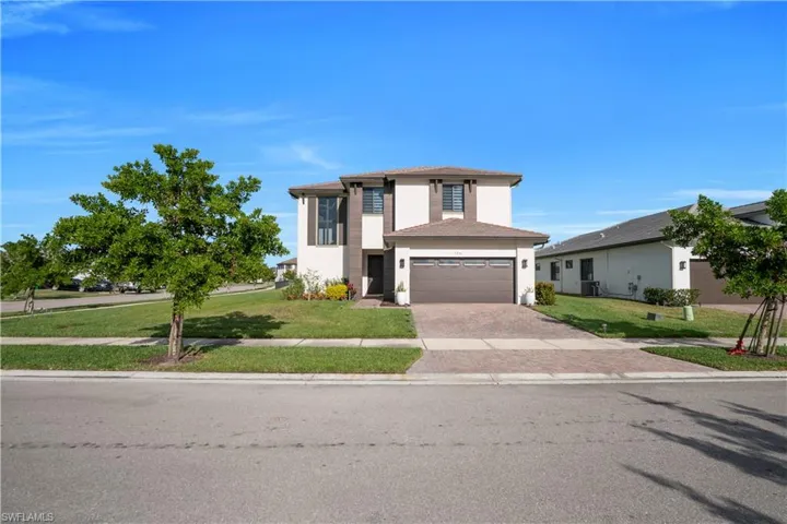 Prairie-style house with a front lawn, decorative driveway, a tile roof, stucco siding, and an attached garage