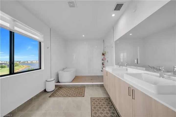 Bathroom featuring double vanity, walk in shower, a freestanding tub, light tile patterned flooring, and a water view