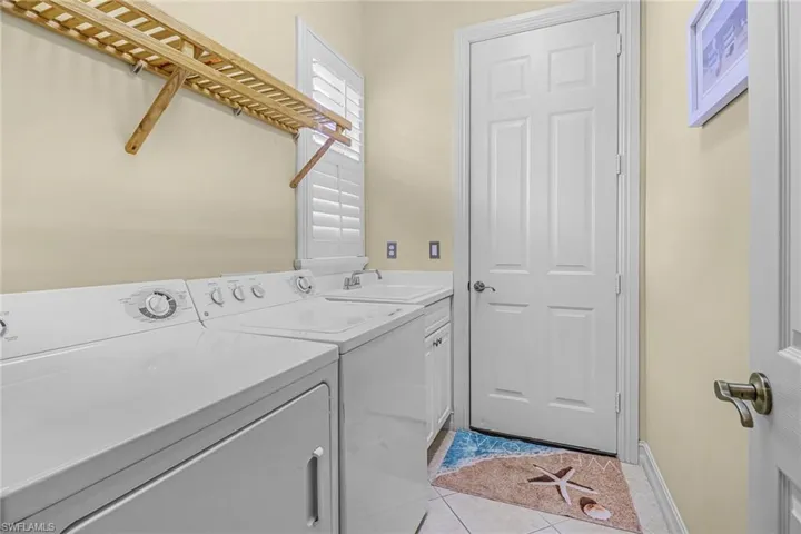 Laundry area featuring sink, separate washer and dryer, light tile flooring, and cabinets