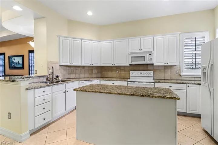 Kitchen featuring white appliances, a kitchen island, light tile floors, sink, and white cabinets