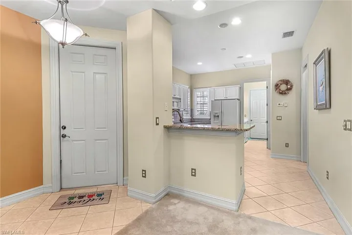 Kitchen with stainless steel fridge, granite counters, white cabinets, kitchen peninsula, and pendant lighting
