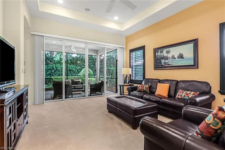 Carpeted living room featuring a tray ceiling and ceiling fan