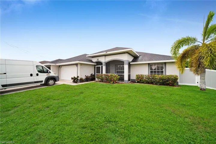 Single-story stucco residence featuring a two-car garage, screened entryway, and a mature palm tree