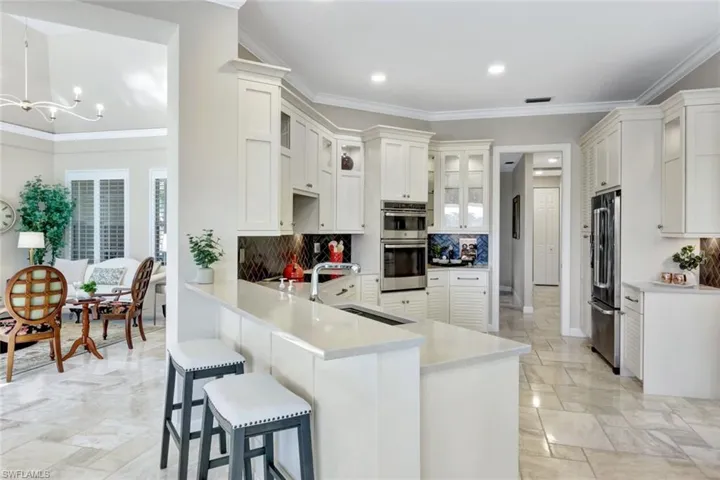 Kitchen featuring kitchen peninsula, appliances with stainless steel finishes, crown molding, sink, and white cabinets