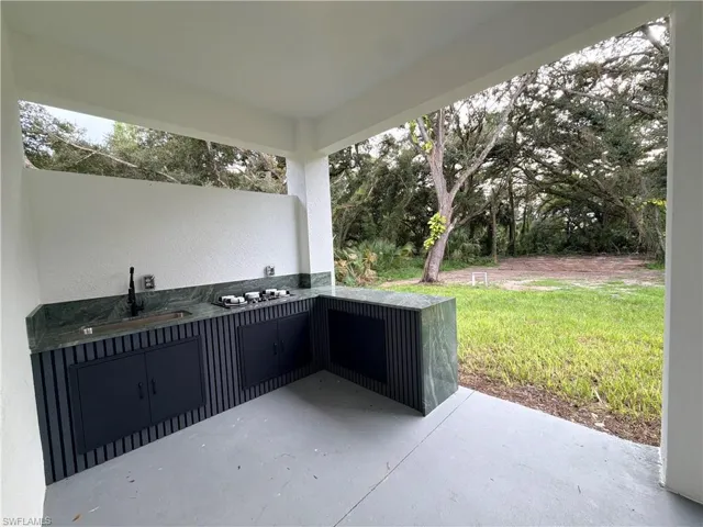 Covered patio with an outdoor kitchen featuring a built-in sink, cooktop, and storage cabinetry