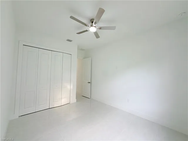 White tile flooring, white walls, white bi-fold closet doors, white interior door, and a ceiling fan with integrated lighting
