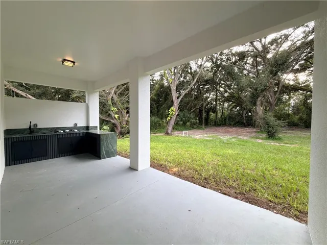 Covered outdoor patio featuring an L-shaped counter with a built-in sink and cooktop, and a natural grass yard