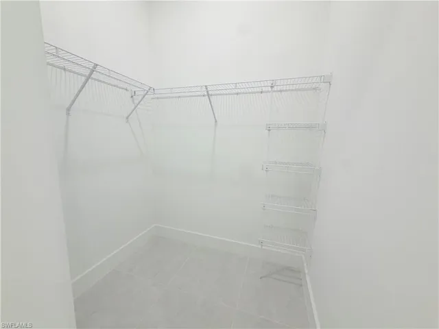 Walk-in closet with L-shaped wire shelving and light gray tile flooring