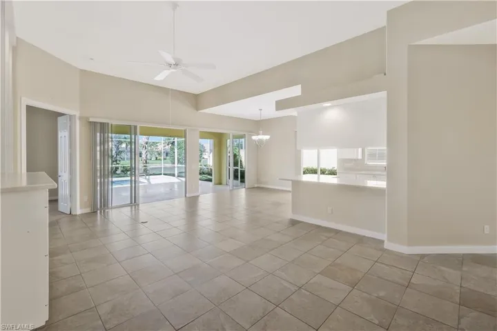Empty room featuring a ceiling fan, light tile patterned floors, a chandelier, and a towering ceiling