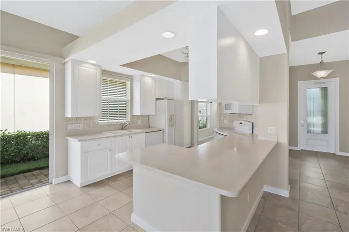 Kitchen with a peninsula, decorative backsplash, white appliances, light countertops, and light tile patterned floors