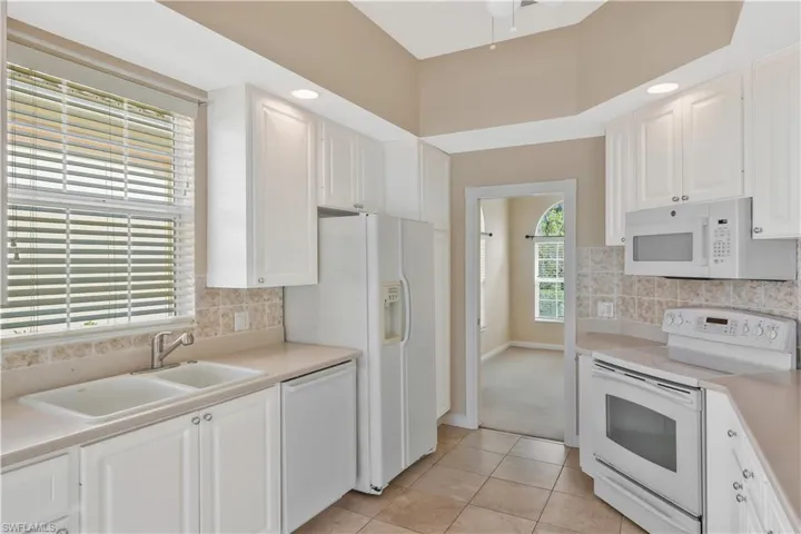 Kitchen with white appliances, backsplash, white cabinets, light countertops, and recessed lighting