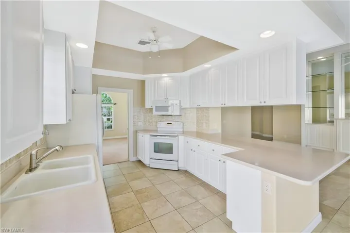 Kitchen featuring backsplash, white cabinets, white appliances, light countertops, and recessed lighting