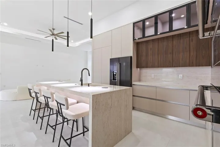 Kitchen featuring high quality fridge, modern cabinets, a breakfast bar area, decorative backsplash, and a kitchen island with sink