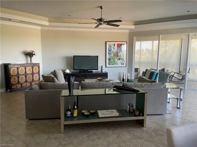 Tiled living room featuring a tray ceiling, crown molding, and ceiling fan