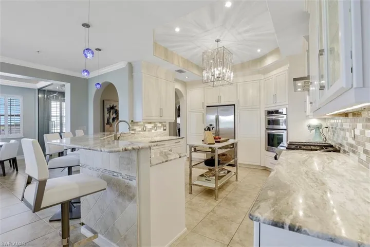 Kitchen with decorative light fixtures, light stone counters, backsplash, stainless steel appliances, and crown molding
