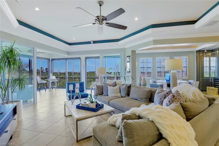 Tiled living room featuring ceiling fan, a raised ceiling, and ornamental molding
