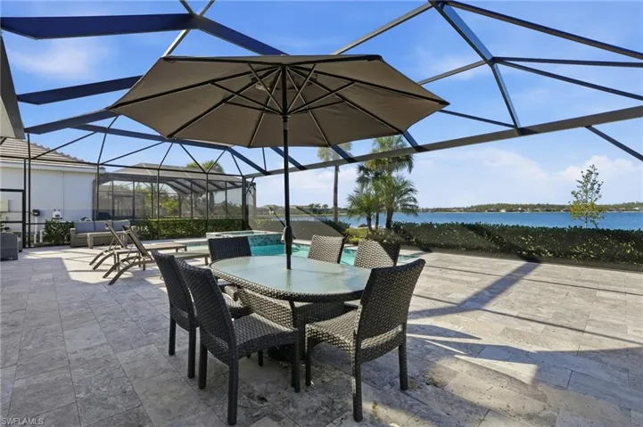 View of patio / terrace featuring glass enclosure, a sunroom, a pool with connected hot tub, outdoor dining area, and a water view