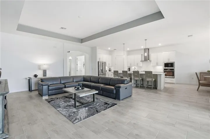 Living area with arched walkways, a raised ceiling, wood finish floors, and recessed lighting