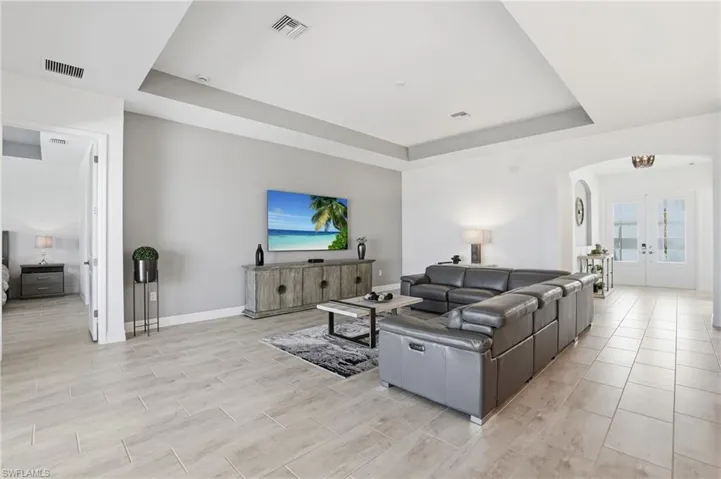 Living room featuring a tray ceiling, arched walkways, french doors, and wood tiled floors