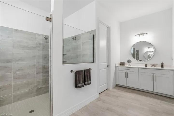 Full bath with walk in shower, double vanity, and light wood-style flooring