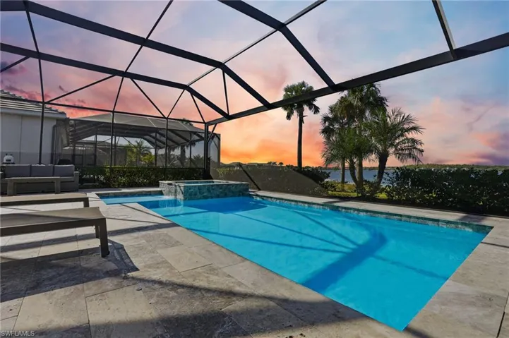 Pool at dusk with a sunroom, a lanai, a pool with connected hot tub, and a patio area