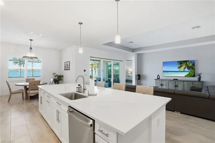 Kitchen with white cabinets, hanging light fixtures, open floor plan, stainless steel dishwasher, and a center island with sink