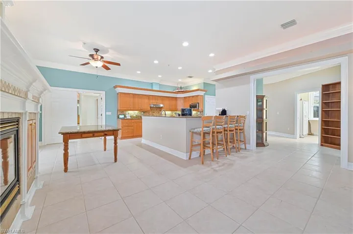 Kitchen featuring a ceiling fan, a peninsula, crown molding, light tile patterned floors, and a fireplace