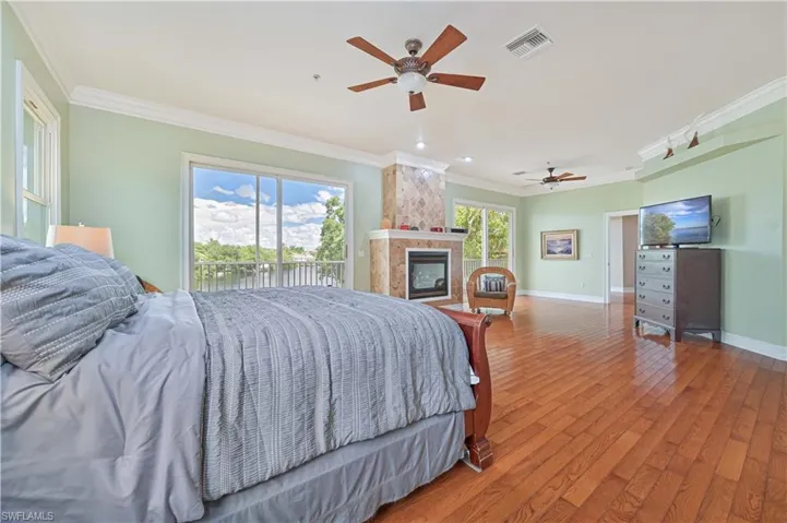 Bedroom with ornamental molding, hardwood / wood-style flooring, a fireplace, access to outside, and a ceiling fan