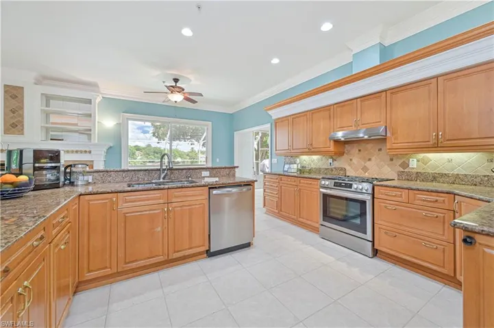 Kitchen featuring stainless steel appliances, under cabinet range hood, a ceiling fan, backsplash, and stone countertops