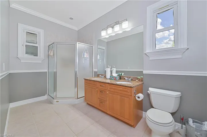 Full bath featuring double vanity, tile patterned floors, a stall shower, and crown molding