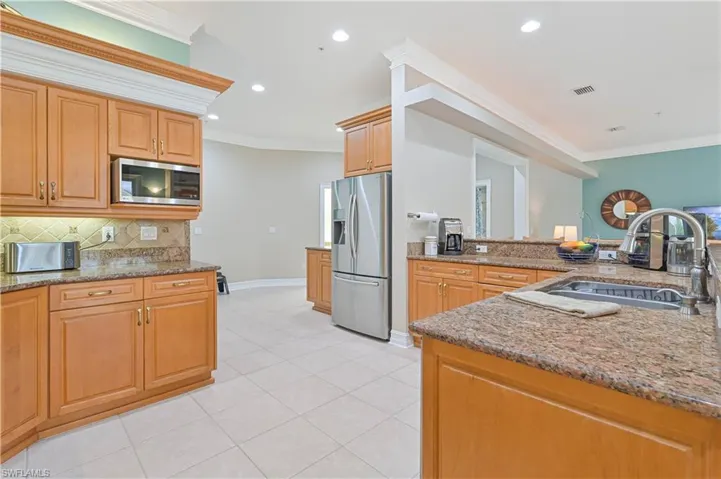 Kitchen with appliances with stainless steel finishes, ornamental molding, decorative backsplash, stone counters, and recessed lighting