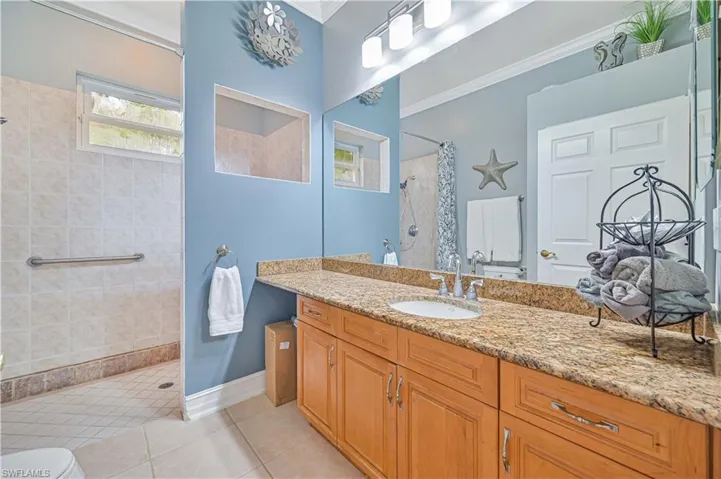 Bathroom with a tile shower, tile patterned flooring, vanity, and ornamental molding