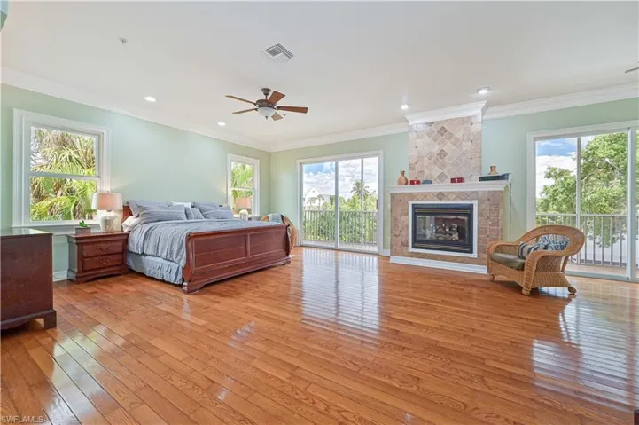 Bedroom featuring light wood-style flooring, access to outside, multiple windows, a tile fireplace, and crown molding