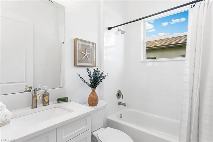 White bathroom featuring an integrated sink vanity with a light-toned countertop, a full-length mirror, a window-equipped tub/shower combination, and white tile surround