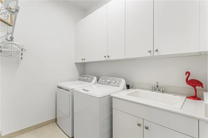 Dedicated laundry area featuring white cabinetry, a utility sink with stainless steel faucet, and tile flooring