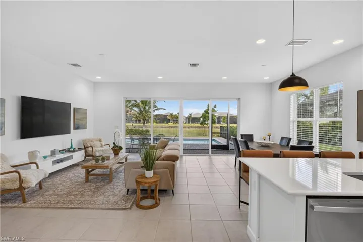 Open-concept living space featuring large format tile flooring, recessed lighting, and expansive sliding glass doors opening to a screened lanai with a pool and water views