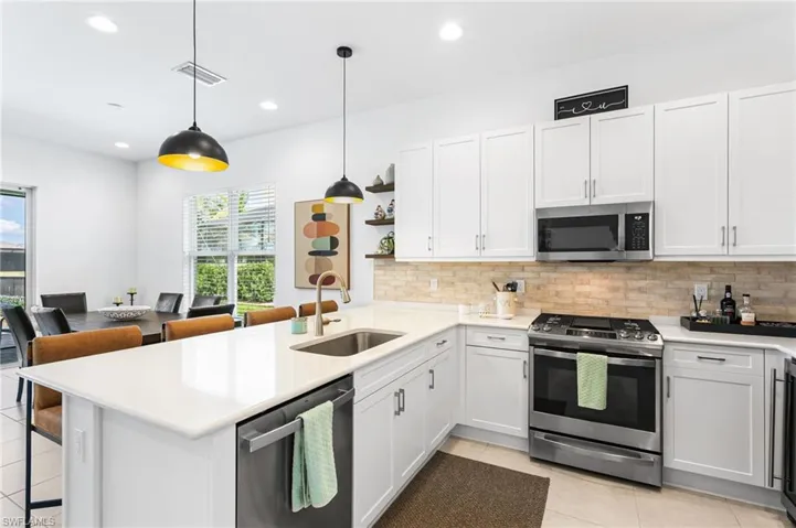 Contemporary kitchen featuring white cabinetry, stainless steel appliances, a light-toned brick pattern backsplash, and a large island with an undermount sink