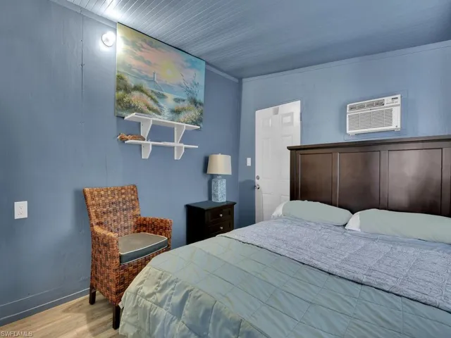 Bedroom with a wall mounted AC, ornamental molding, and light hardwood / wood-style flooring