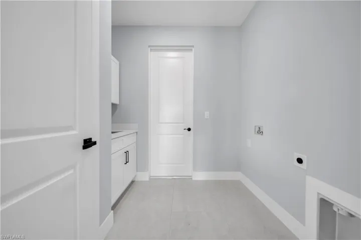 Recessed laundry area with white cabinetry, countertop space, and tiled flooring