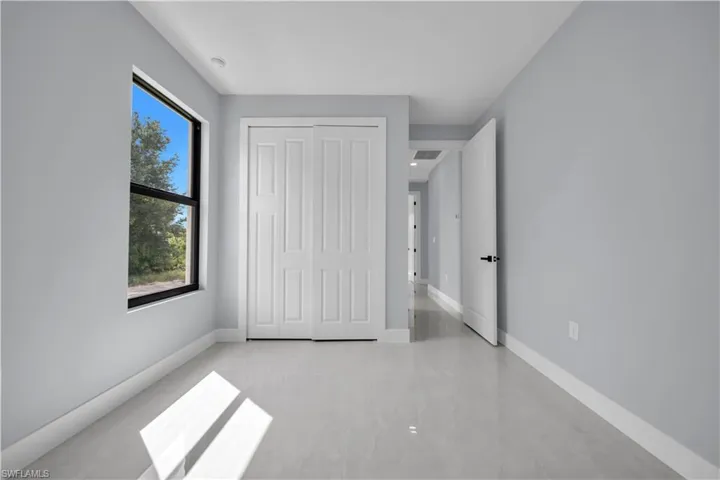 Window with exterior scenery, paneled closet doors, light gray wall finishes, white trim, and polished tile flooring