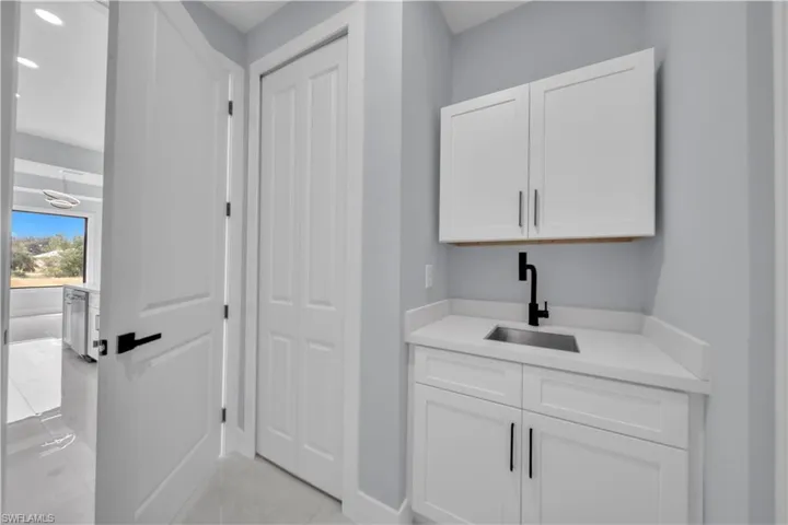 White cabinetry with matte black hardware, stainless steel sink, and a black wall-mounted faucet