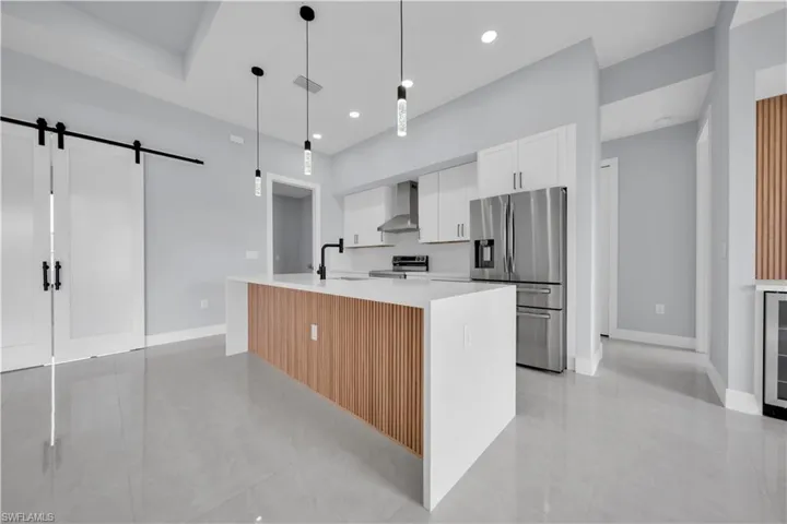 Open-concept kitchen with a large central island, white shaker cabinetry, stainless steel appliances, and contemporary pendant lighting