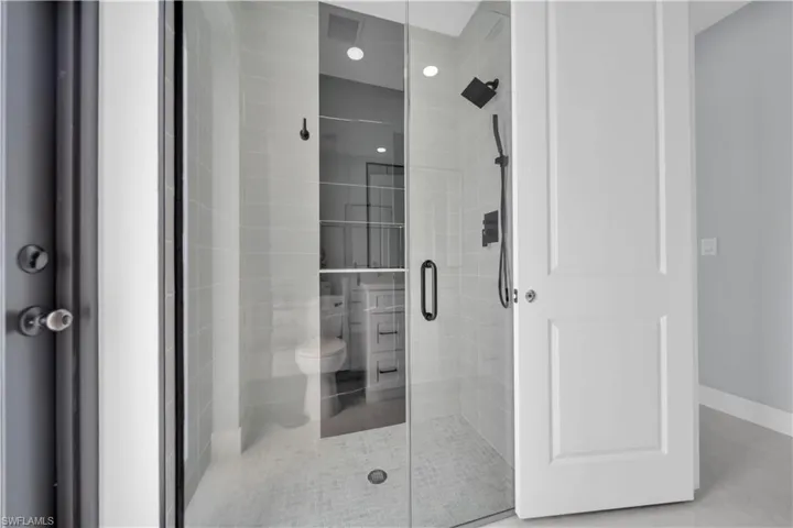 Frameless glass shower enclosure with matte black fixtures, light subway tile surround, recessed lighting, and a white paneled door