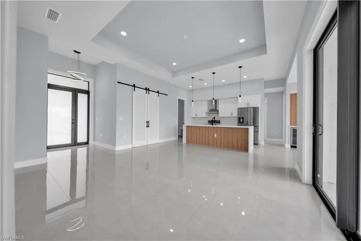 Recessed lighting, tray ceiling, kitchen island with wood-finish paneling, white shaker cabinetry, and large format tile flooring