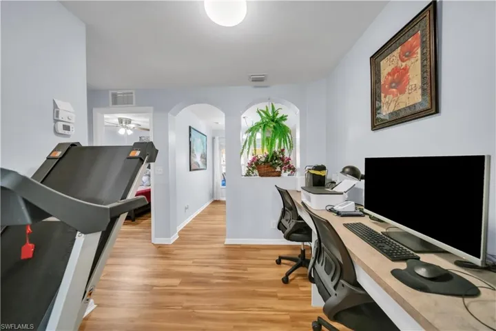 Office space with light wood finished floors, a ceiling fan, and arched walkways